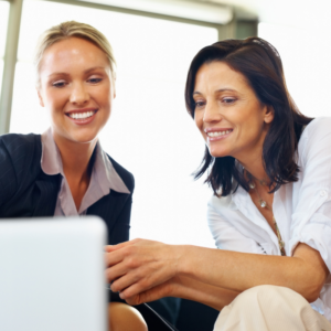 two woman smiling while looking at a computer screen